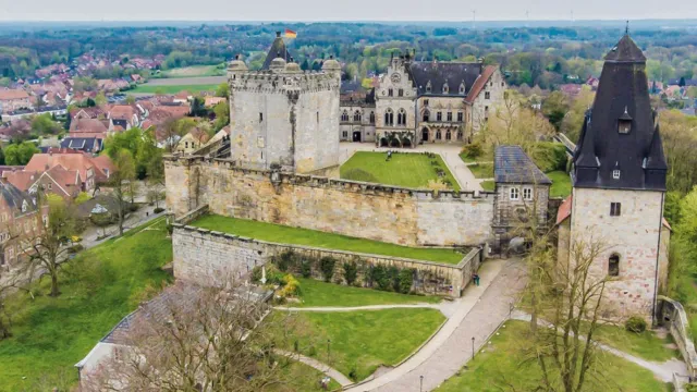 Aerial view of a historic castle with surrounding greenery and distant village.