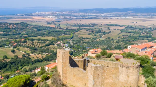 Old stone castle overlooking vast, lush countryside under a clear blue sky.