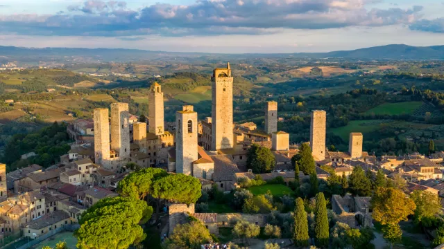 Medieval town with tall towers under a blue sky, surrounded by lush countryside.