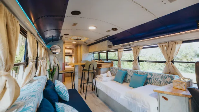 Converted bus interior with blue accents, couches, and a small dining area.