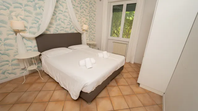 Cozy bedroom with a double bed, white curtains, and patterned wallpaper.