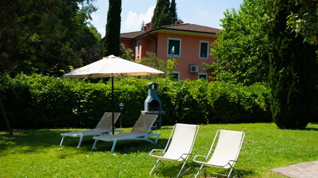 Lawn with lounge chairs and an umbrella near a red house surrounded by greenery.