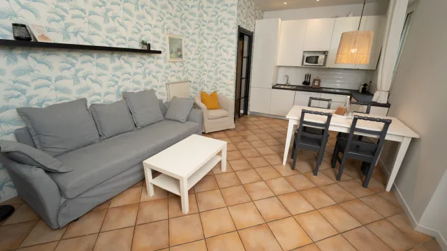 Living room with gray sofa, white table, dining set, and kitchen in background.
