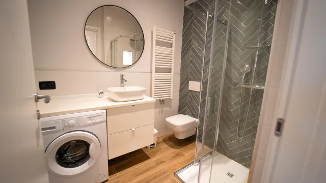 Modern bathroom with a shower, washing machine, and round mirror.