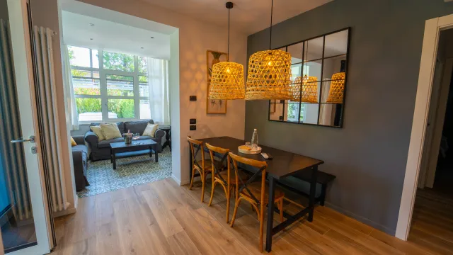 Dining area with wooden table, wicker chairs, pendant lights, and adjacent cozy living room.