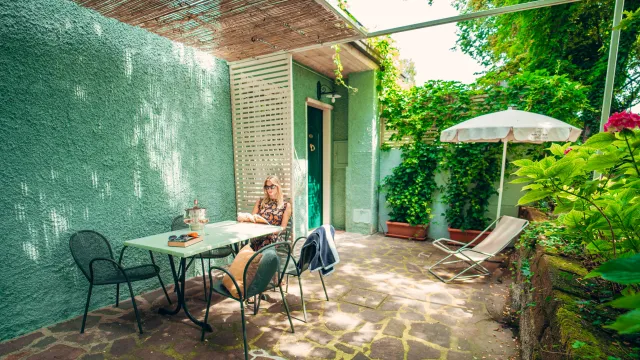 Cozy patio with green walls, a small table, chairs, and plants in sunlight.