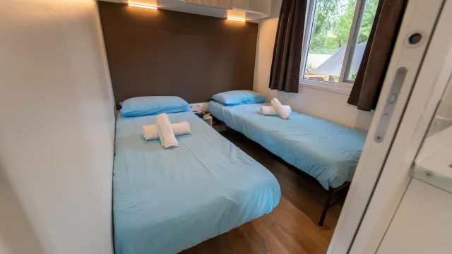 Two single beds with blue sheets in a small, bright room.