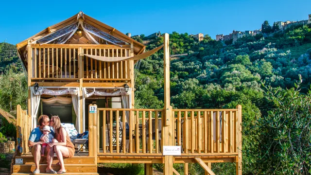 Air lodge with people seated, set against a green hillside under a blue sky.