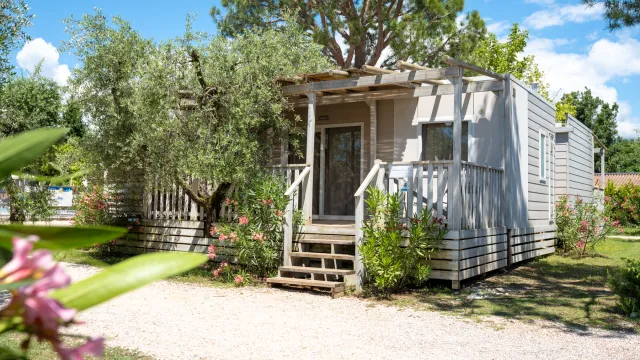 Cozy cabin with porch, surrounded by greenery and flowers under a blue sky.