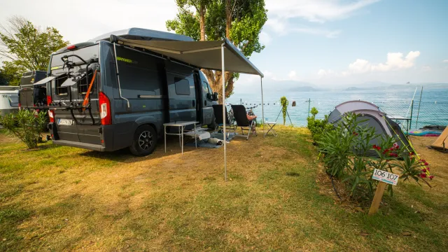 Campervan and tent on grassy lakeside campsite under clear blue sky.
