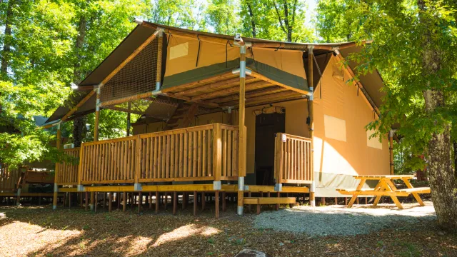 Yellow tent cabin with wooden deck in a sunny, green forest setting.