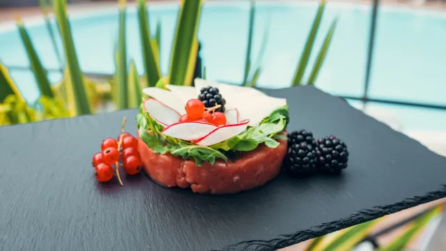 Savory appetizer with radish and berries on slate near a pool.