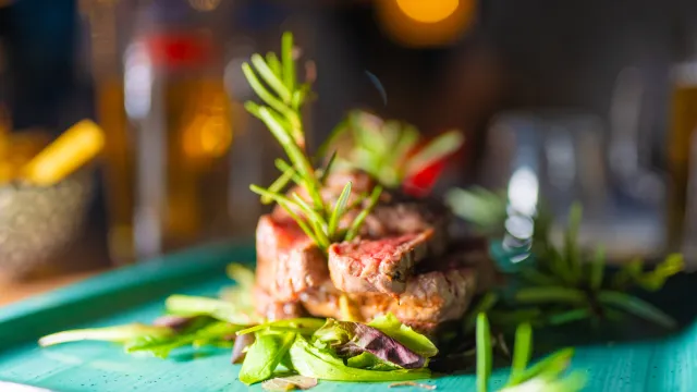 Steak garnished with rosemary on a green plate, blurred background.