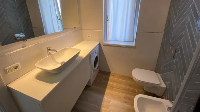 Modern bathroom with sink, mirror, and toilet; wooden floor; herringbone tiles.