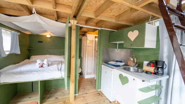 Cozy cabin interior with bed and compact kitchen, wooden ceiling and green accents.