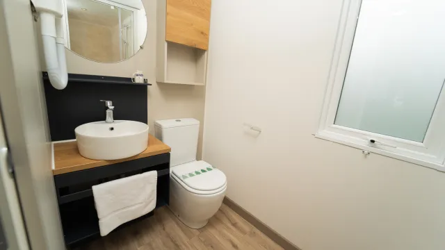 Clean bathroom with a round mirror, white sink, and toilet next to a window.