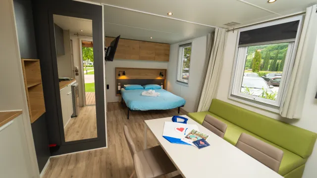 Modern hotel room with a double bed, table, and sofa. Bright natural light.
