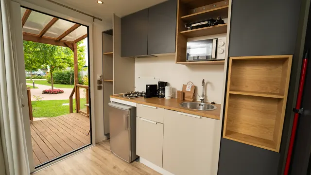 Compact modern kitchen in a small cabin with an open door to a deck outside.