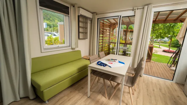 Cozy room with green sofa, table, and large windows opening to a garden view.