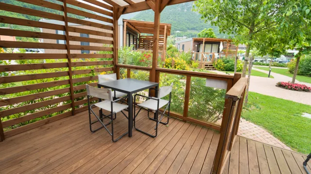 Deck with table and chairs, surrounded by greenery and trees.