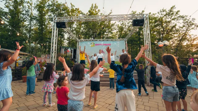 Children dancing joyfully at an outdoor event under string lights.