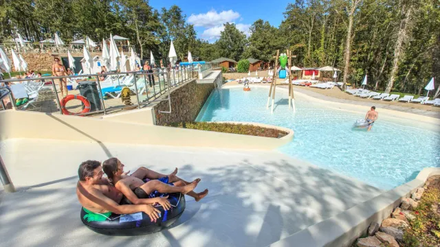 People on inner tubes near a lazy river in a wooded water park.