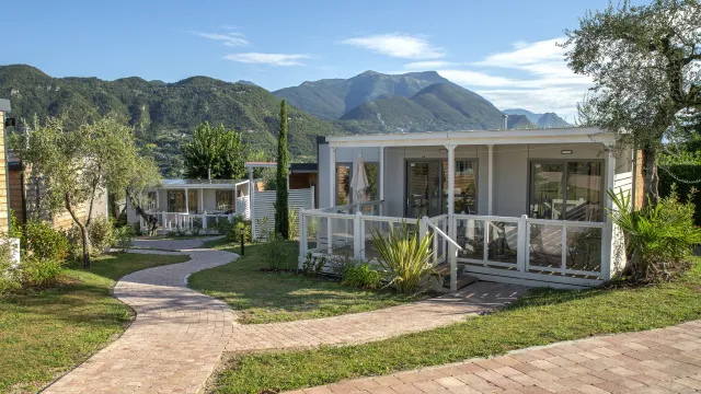 Curved pathway leads to cottages with mountain backdrop under clear blue sky.
