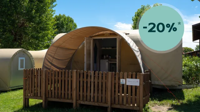 Camp tent with wooden fence, sunny day, trees in background.