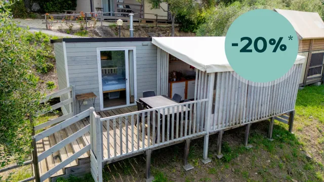 Photograph of a small cabin with a wooden deck in a green setting.