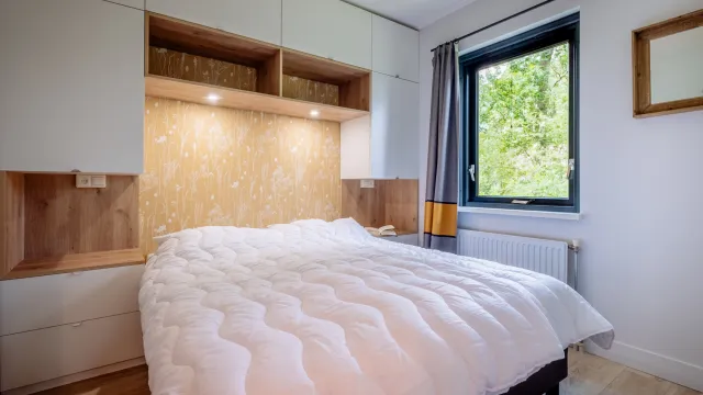 Cozy bedroom with a white quilted bed, window view, and decorative wood paneling.