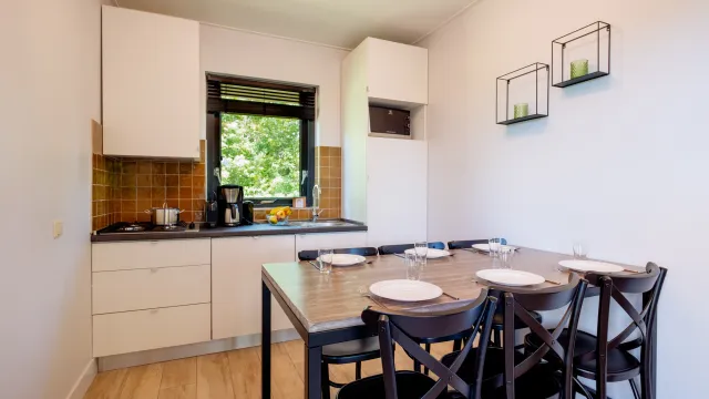 Kitchen with a dining table set for four, white cabinets, and a window view of greenery.