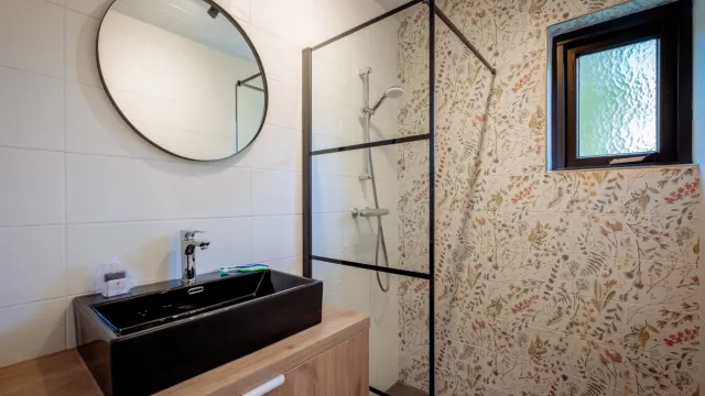 Modern bathroom with round mirror, black sink, and glass shower enclosure.