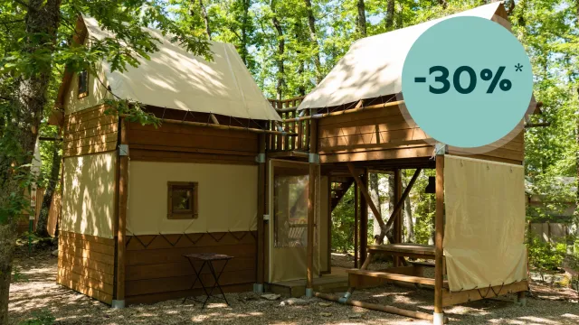 Wooden glamping cabin in a forest setting, shaded by trees.