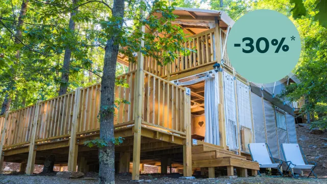 Wooden cabin in a forest with deck chairs outside.