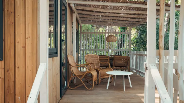 Cozy veranda with wicker chairs, sofa, and a white table under a pergola.