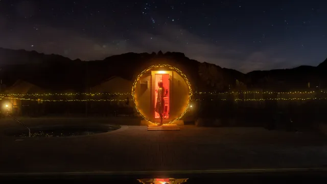 Red-lit phone booth in a starry night landscape, surrounded by mountains.