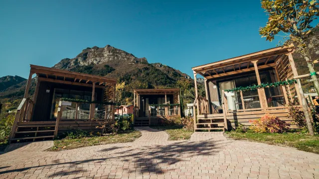 Cabins with wooden porches, mountain backdrop, clear sky.