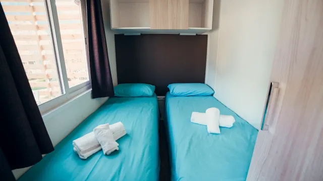Twin beds with blue sheets and folded towels in a bright room.
