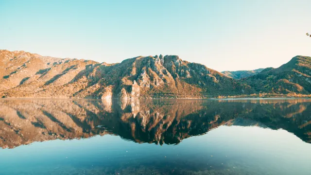 Calm lake reflecting mountains under clear blue sky.