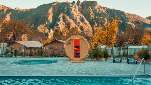 Mountain resort with pool, hot tub, and barrel sauna at sunset.
