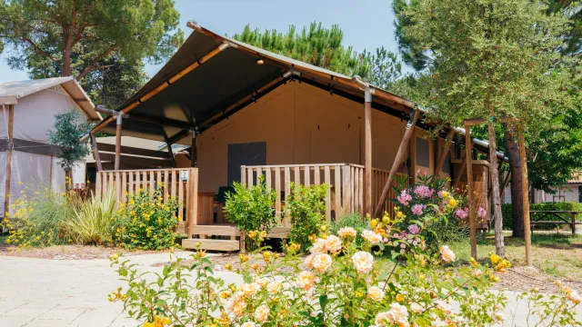 Tent cabin with wooden deck in a garden, surrounded by blooming flowers and trees.