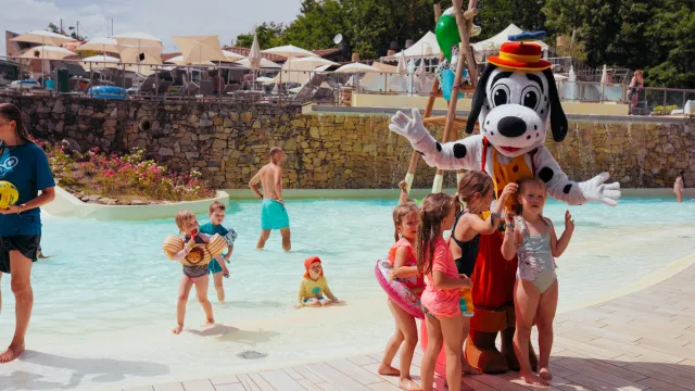 Kids posing with a tall cartoon character by a pool in a water park.