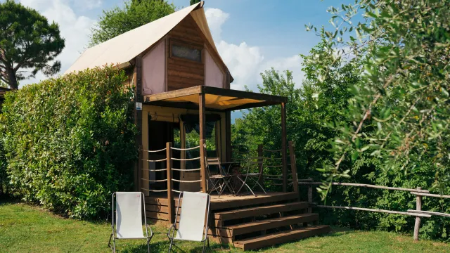 Rustic wooden cabin with a sloped roof, surrounded by greenery. Two chairs in front.