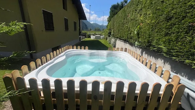 Hot tub in a garden, surrounded by a wooden fence, sunny day.