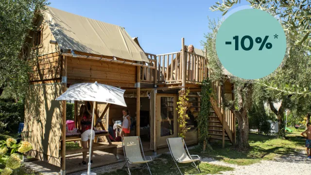 Wooden cabin with patio chairs, umbrella, and greenery under clear blue sky.