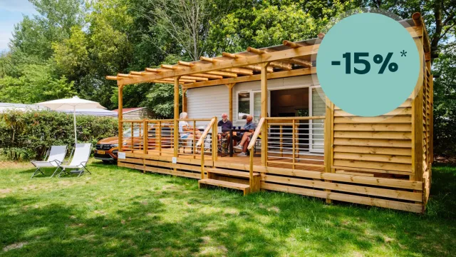 Wooden cabin with porch, surrounded by greenery, sunny day.