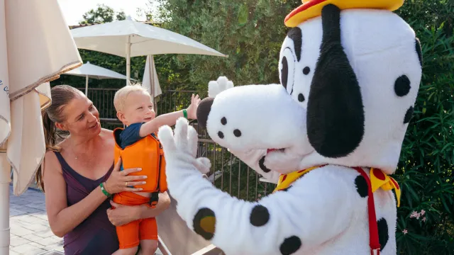Kind hoog-fives persoon in een Dalmatiër-mascotte kostuum bij het zwembad, vastgehouden door lachende volwassene.