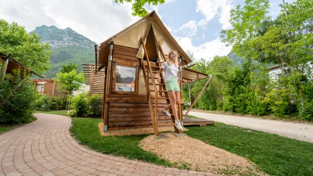 Une cabane en bois dans un environnement montagneux luxuriant avec un ciel bleu et des nuages.
