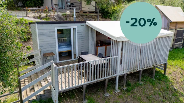 Small cabin with deck in a wooded area, discount badge displayed.