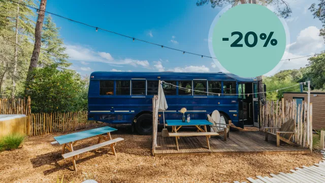 Blue bus on a sunny campsite with picnic tables under string lights.